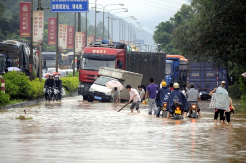 5月18日，國道324線廣西興業縣石南鎮黑石嶺路段被洪水淹沒，一名群眾手持木棍為摩托車探路。