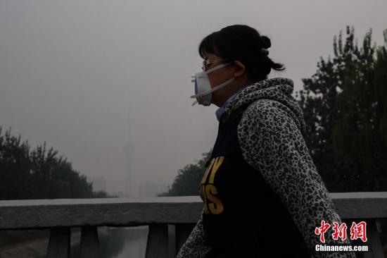 資料圖：北京一名市民戴防霾口罩在戶外行走，遠處的中央電視塔亦被霧霾籠罩。<a target='_blank' href='http://www.chinanews.com/'>中新社</a>記者 崔楠 攝